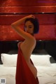 A woman in a red dress standing on a bed.