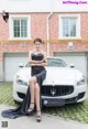 A woman in a black dress sitting on the hood of a white car.