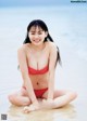 A woman in a red bikini sitting on the beach.