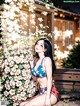 A woman in a bikini sitting on a bench next to a bush of flowers.