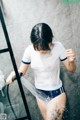 A woman in a white shirt and blue shorts is taking a shower.