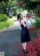 A woman in a black dress standing under a tree.