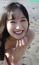 A young woman sitting on a sandy beach with her hand on her chin.